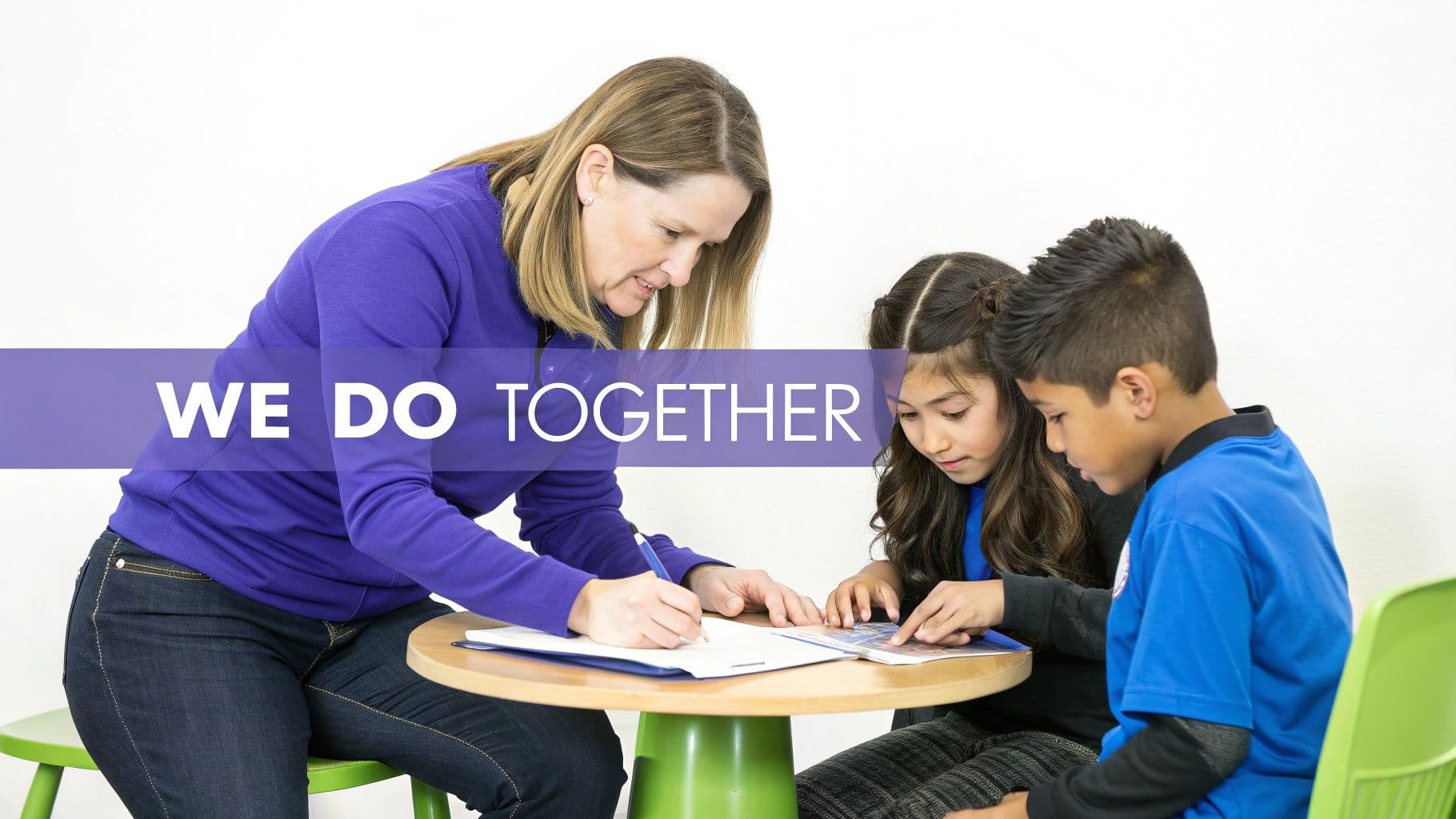 A female teacher helps two children, a girl and a boy, with their schoolwork at a small table.