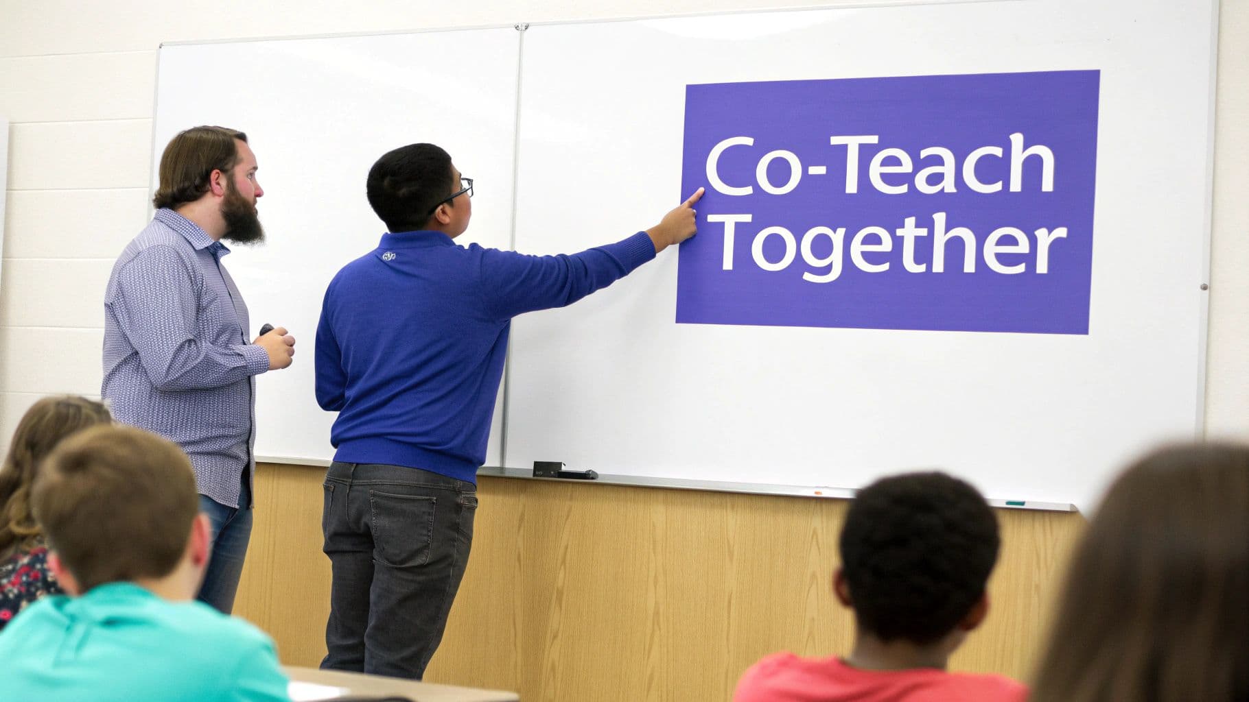 Two instructors lead a session on co-teaching, pointing to a 'Co-Teach Together' sign on a whiteboard.