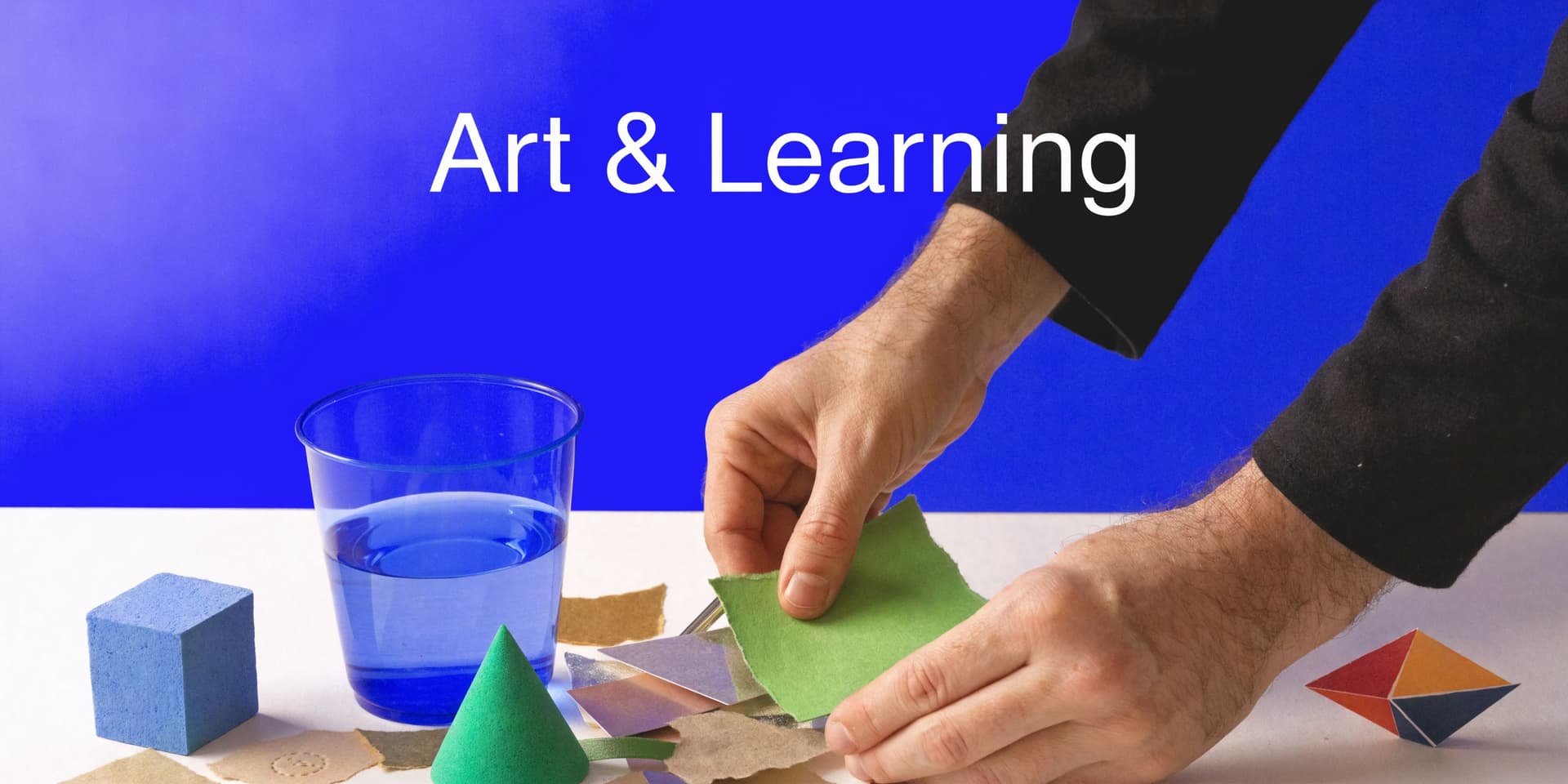 A person crafting with geometric shapes, colorful paper, and a blue water cup on a table.