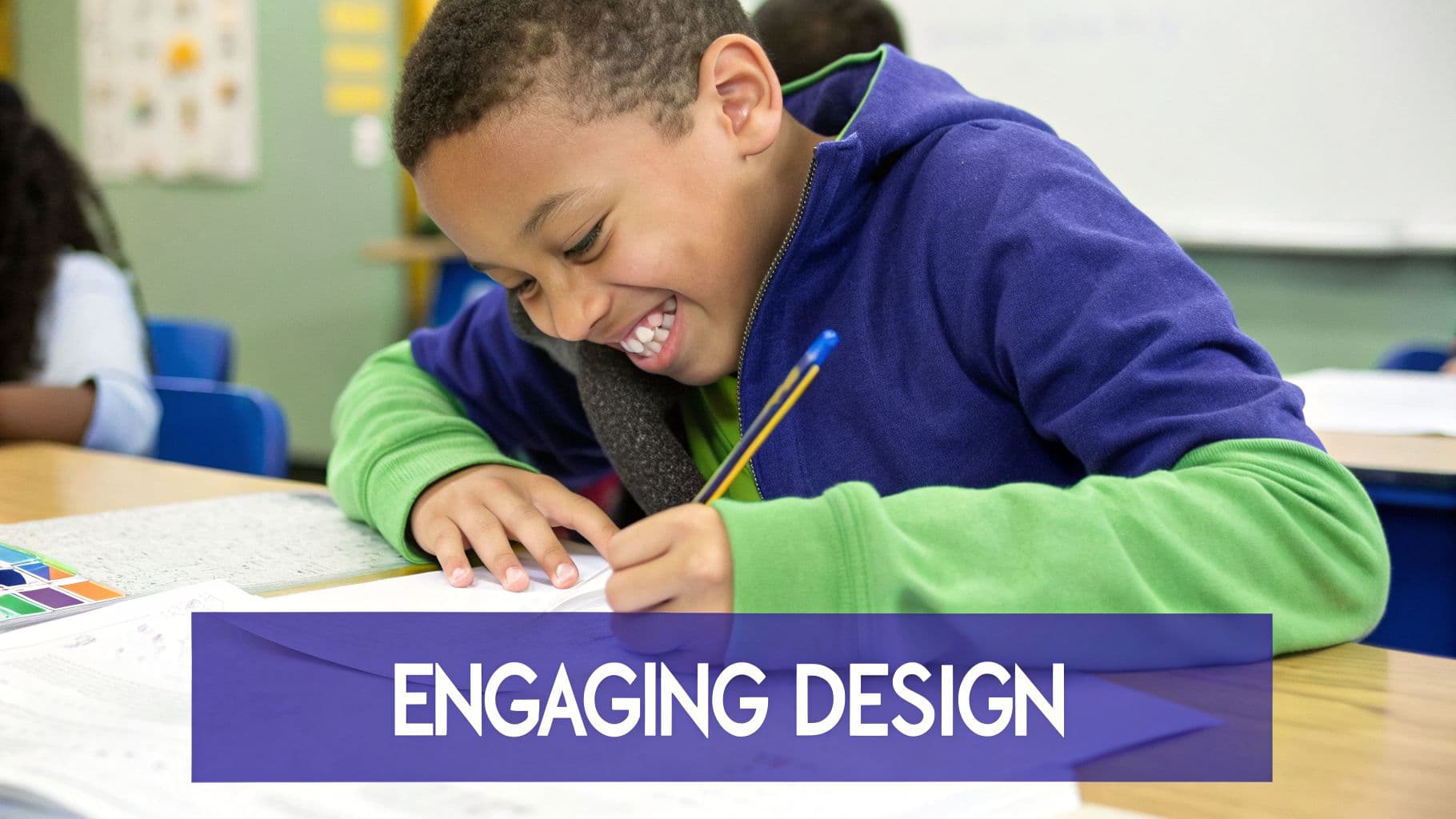 A happy young boy in a blue hoodie smiles broadly while writing with a pencil at a school desk.