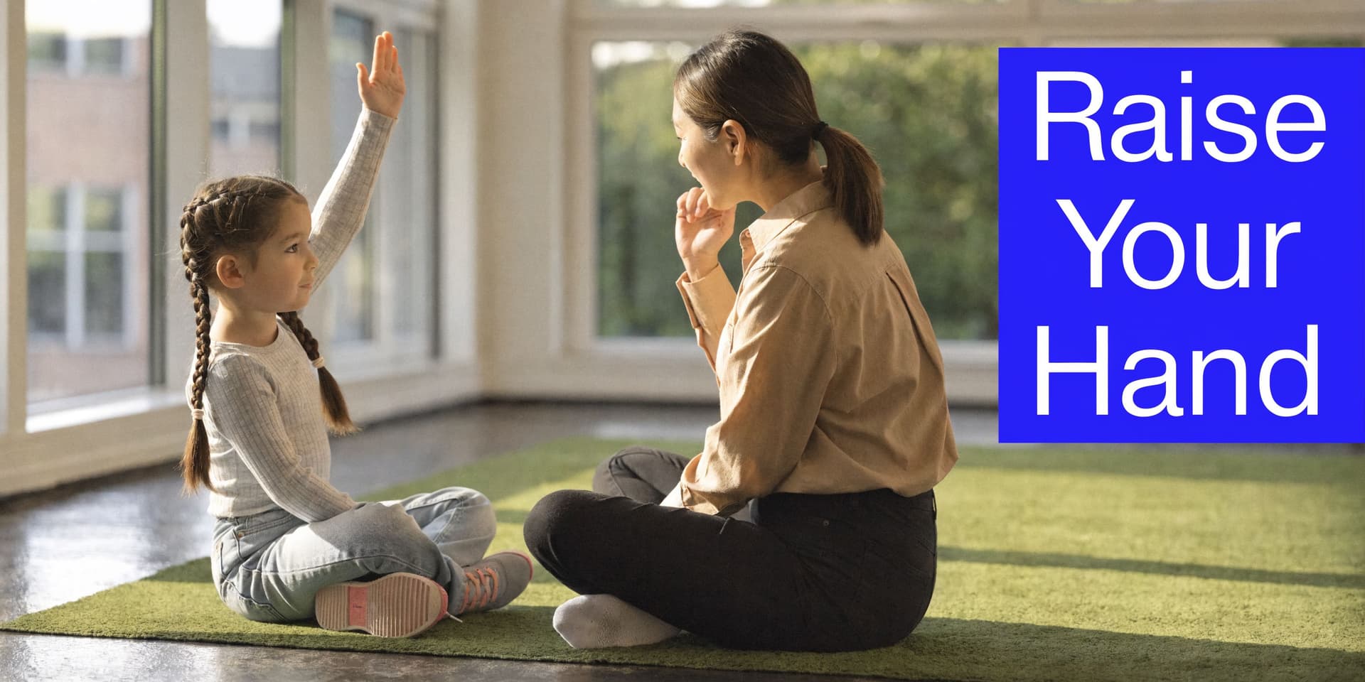 A young girl with braided hair raises her hand while sitting on a rug with her teacher.
