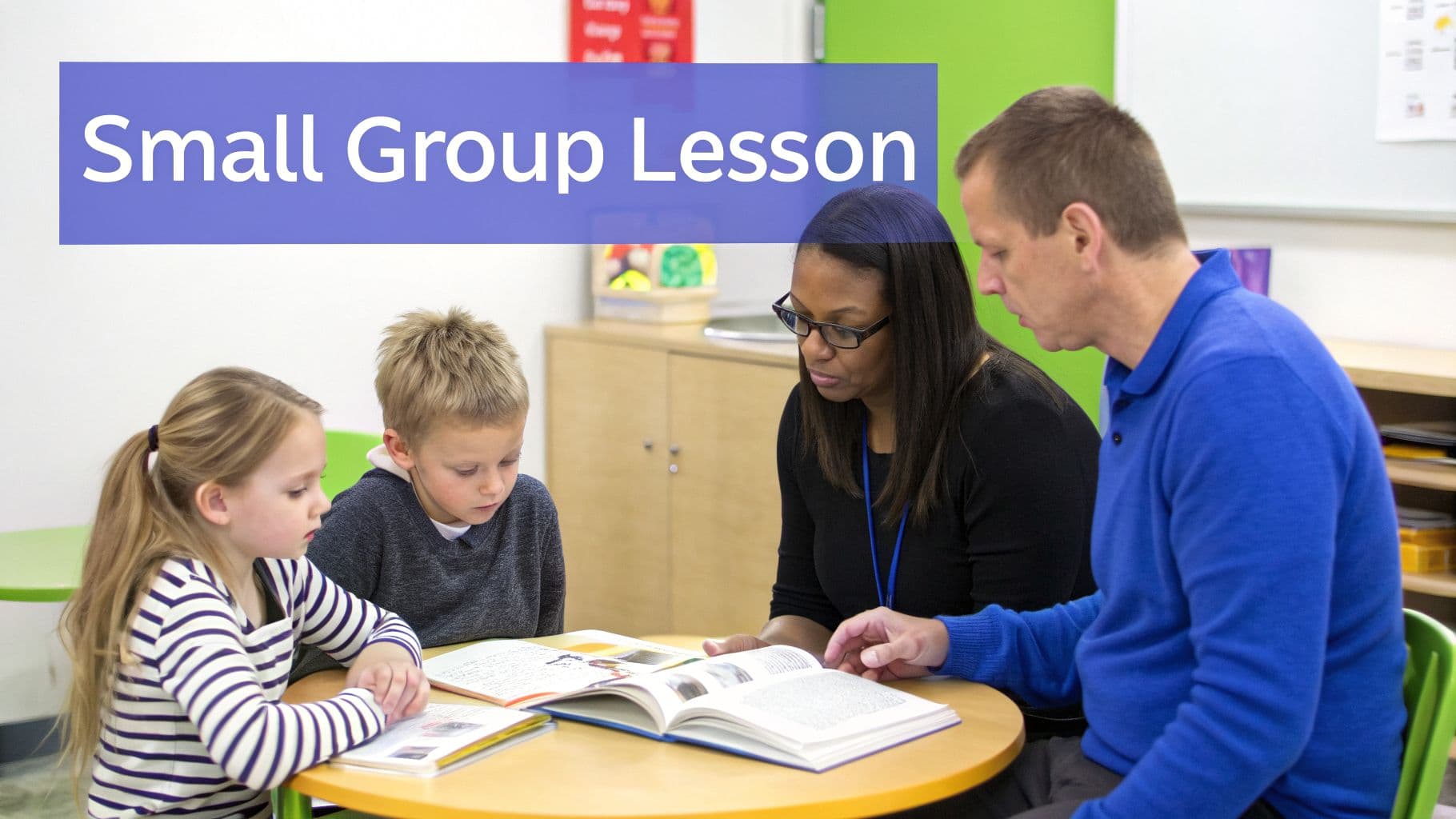 Two adults and two children sit at a table, engaged in a small group reading lesson.