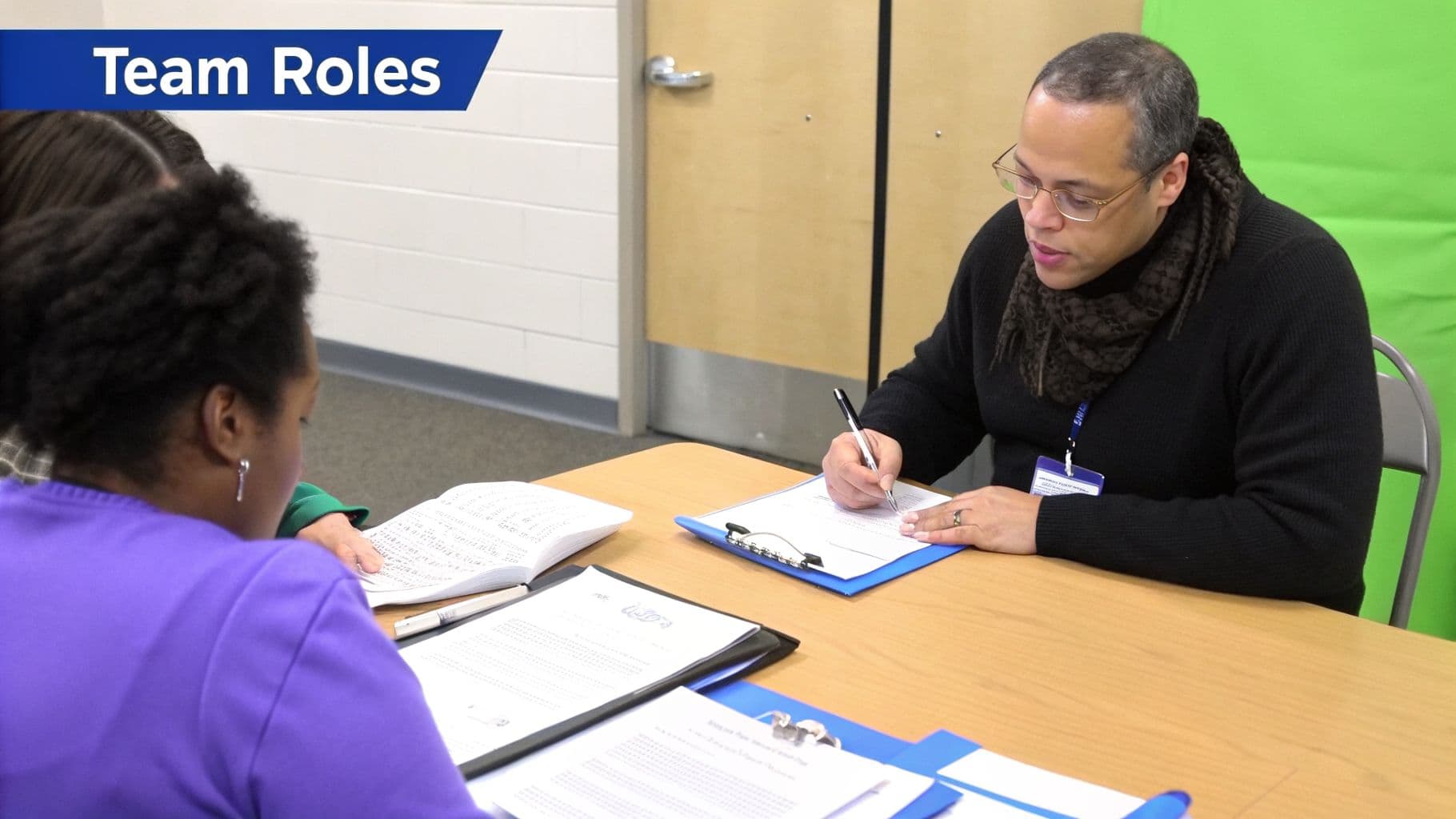 A man and two women at a table working on documents under a 'Team Roles' banner.